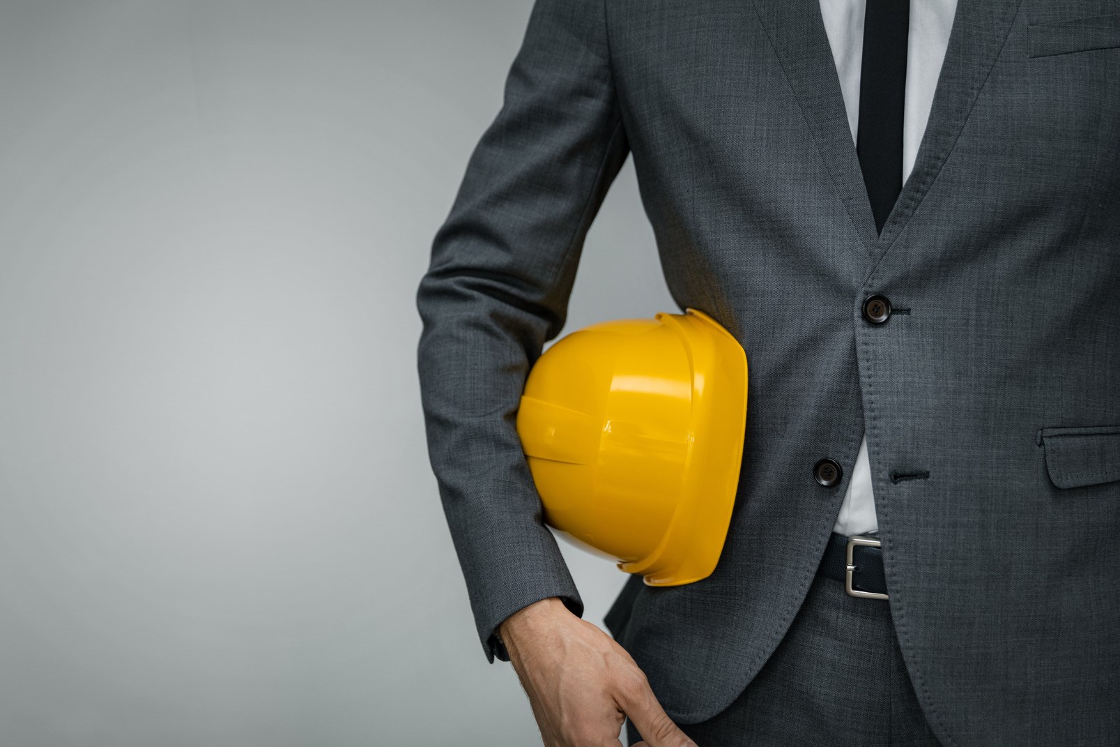 Construction industry business - businessman holding yellow hard hat underarm on gray background with copy space