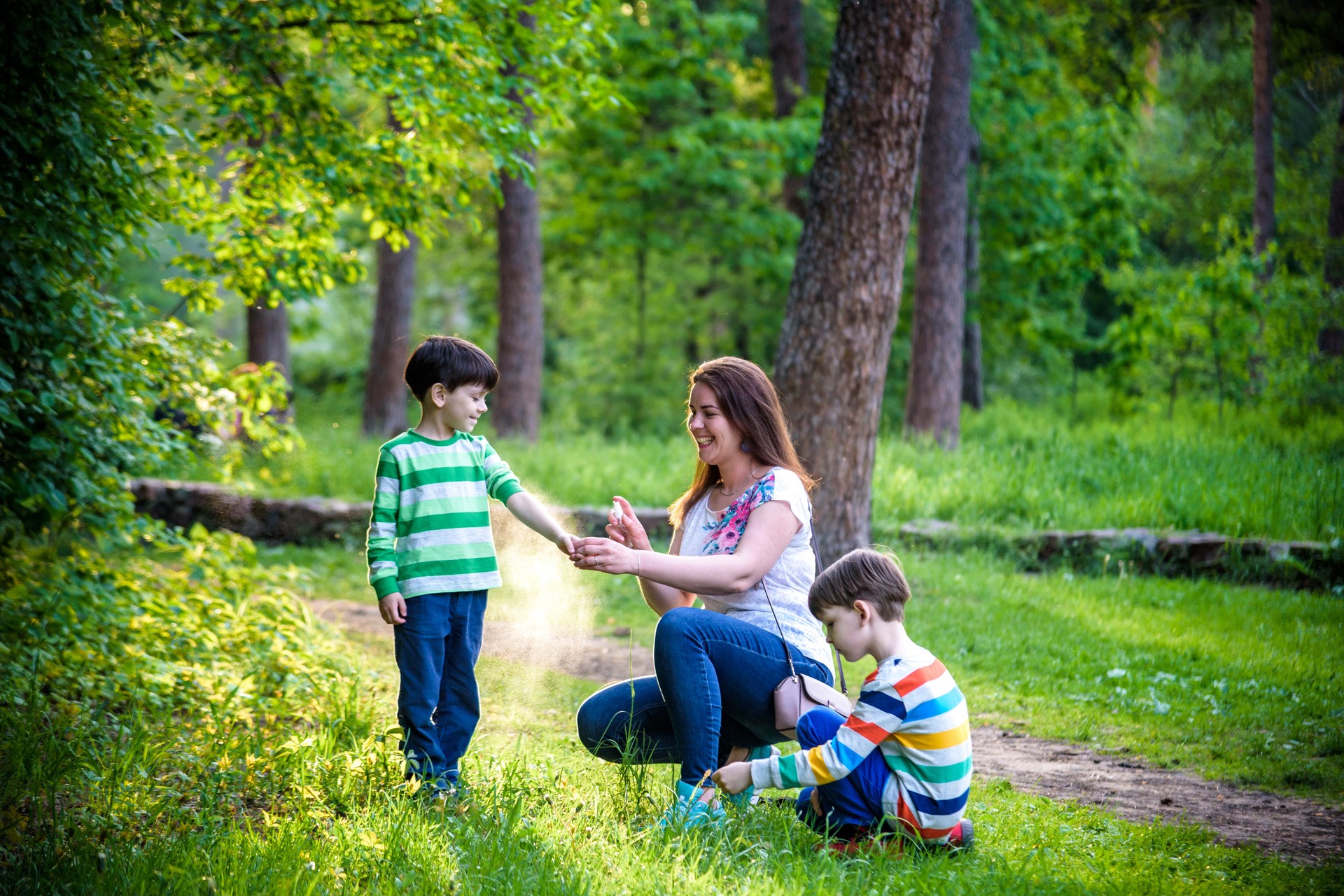 Young woman mother applying insect repellent to her two son before forest hike beautiful summer day or evening. Protecting children from biting insects at summer. Active leisure with kids