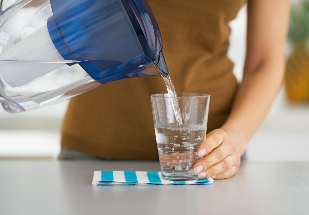 Nahaufnahme der Hausfrau, die Wasser aus dem Wasserfilterkrug in das Glas gießt.
