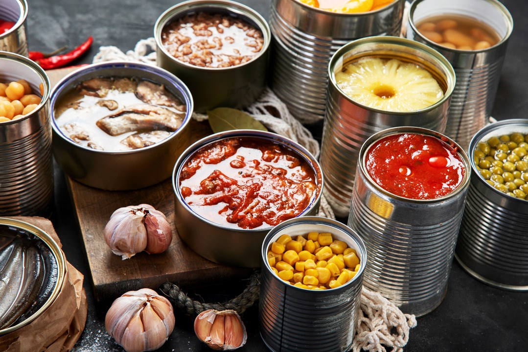Gemüse-, Bohnen-, Fisch- und Obstkonserven in Blechdosen auf schwarzem Hintergrund. Lebensmittelvorräte.
