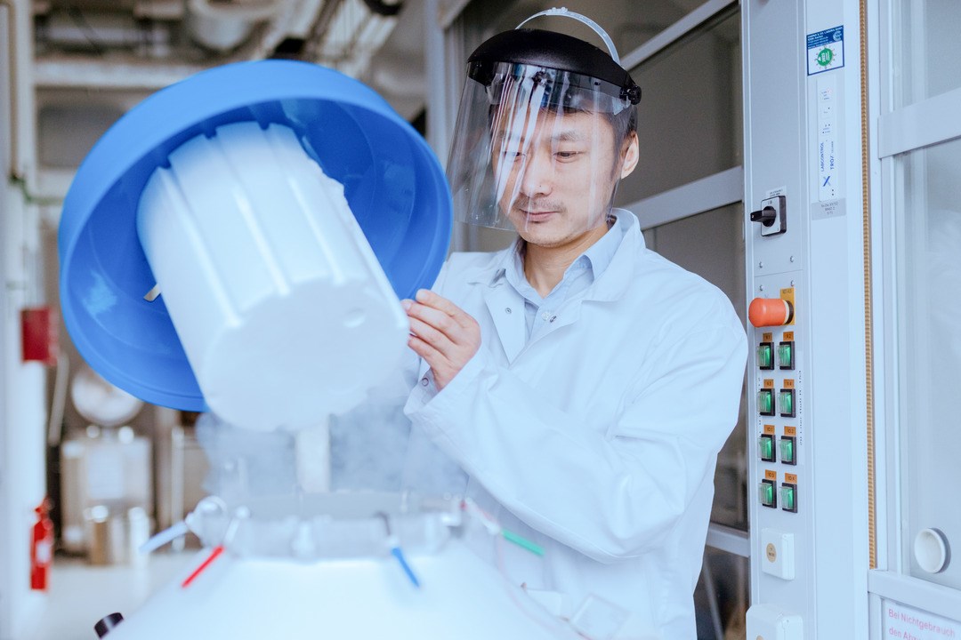 Lab technician wears protective visor and works with a blue hood in the lab. Wei Xie