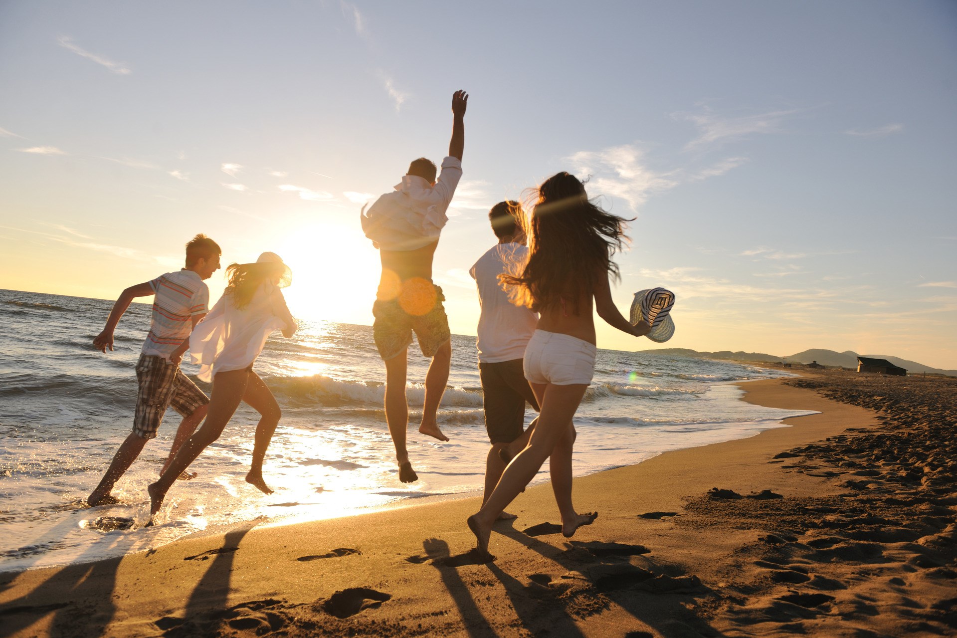 group of young people having fun running and jumping on the beach at sunset time