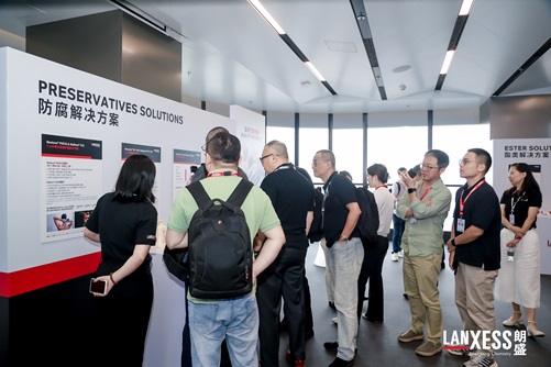 Photo taken during LANXESS Solution Day in Shanghai, China, showing a group of customers gathered around LANXESS employees at an indoor product exhibition area. The customers are listening attentively as LANXESS employees explain the company’s product portfolio, product features, technical information and application solutions. Several participants are standing close to the exhibition panels, reading the displayed product information and engaging with the explanations. Some attendees appear to be observing the presentation closely, while others look at the product displays or interact with the LANXESS representatives. One participant is holding a smartphone, possibly taking a photograph of the exhibition or the displayed information.
The scene captures an interactive, customer-focused product presentation during LANXESS Solution Day in Shanghai. It illustrates direct communication between LANXESS employees and customers, with participants exploring the company’s product offerings, learning about relevant solutions and exchanging information in a professional exhibition setting. The bright, modern indoor venue, exhibition booths and small-group discussion create an atmosphere conducive to technical communication, customer engagement and knowledge sharing. The photograph documents LANXESS’s engagement with customers and its efforts to present its product solutions and technical expertise in person.